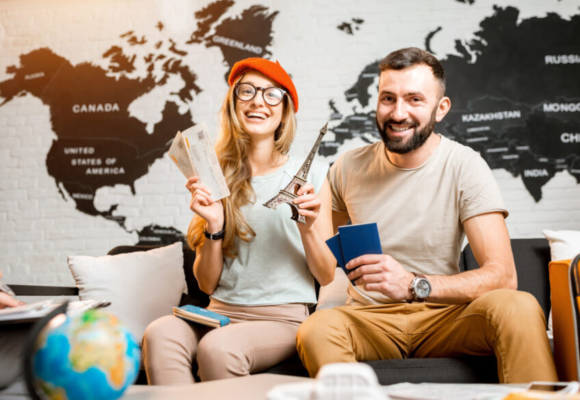 Young couple sitting with eiffel tower at the travel agency office on the world map background prepairing for a trip to Paris